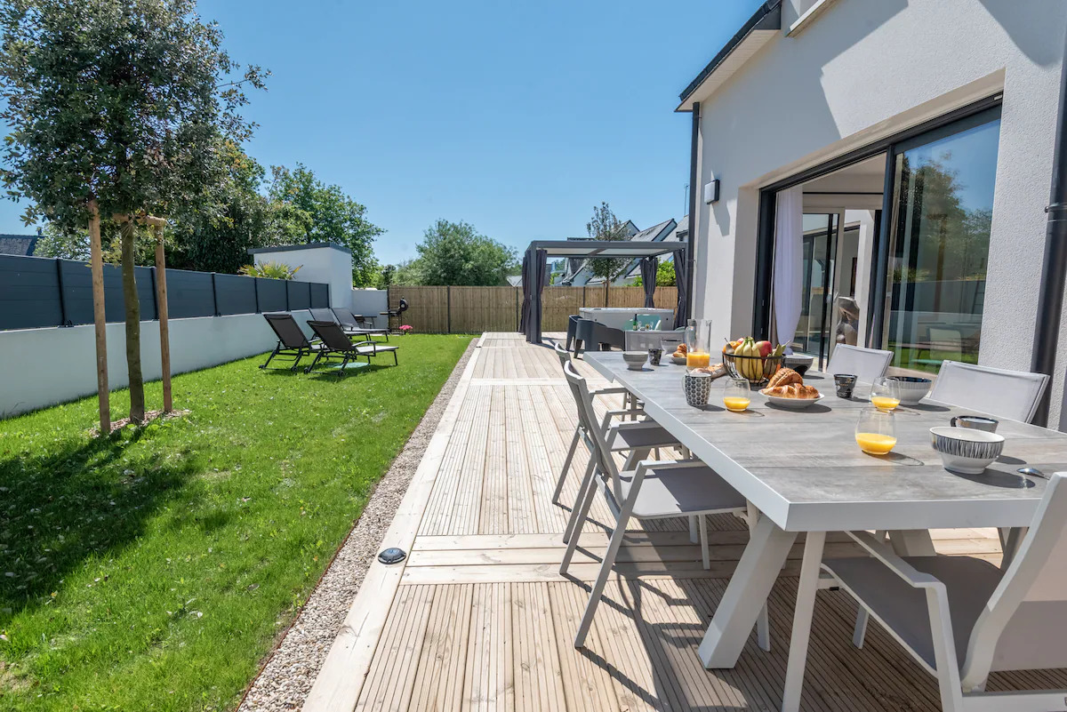 Villa à Erdeven dans le Morbihan ouverte sur le jardin et la terrasse de 90 m², équipée d’une table pour 10 personnes, deux grands parasols, un petit salon extérieur et un SPA. Les grandes baies vitrées donnent un accès direct sur le jardin et la terrasse qui sont visibles depuis toutes les pièces.